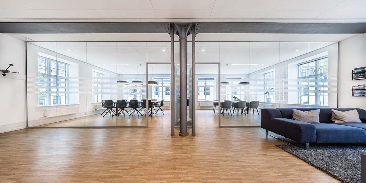 Lyst loungeområde, glasvægge, åbne kontormiljøer og eksklusive fællesfaciliteter.
